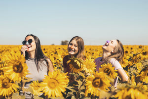 Three girl friends wearing colorful Nöz zinc oxide sunscreen and laughing in a sunflower field